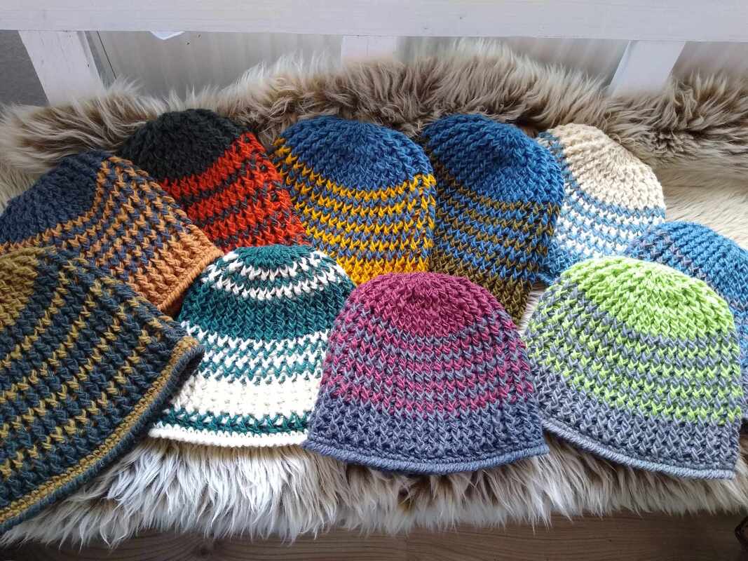 Verschiedene gehäkelte Mützen in bunten Farben für Damen, Herren und Kinder auf einer Fellunterlage