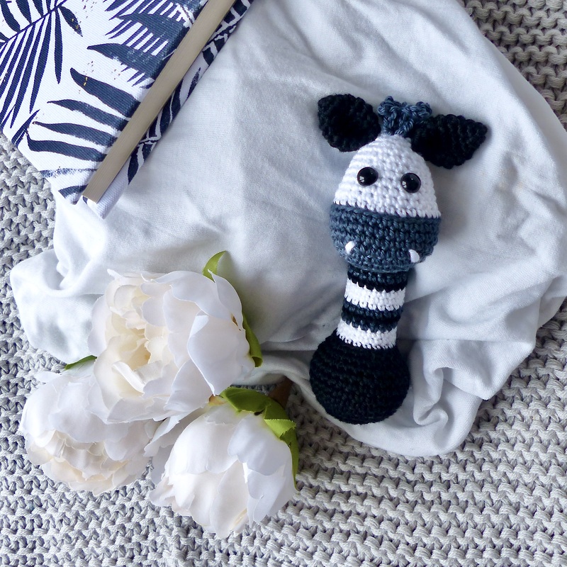 Zarter gehäkelter Greifling in Schwarz-Weiß mit Tierkopf auf Stoff und Blumen