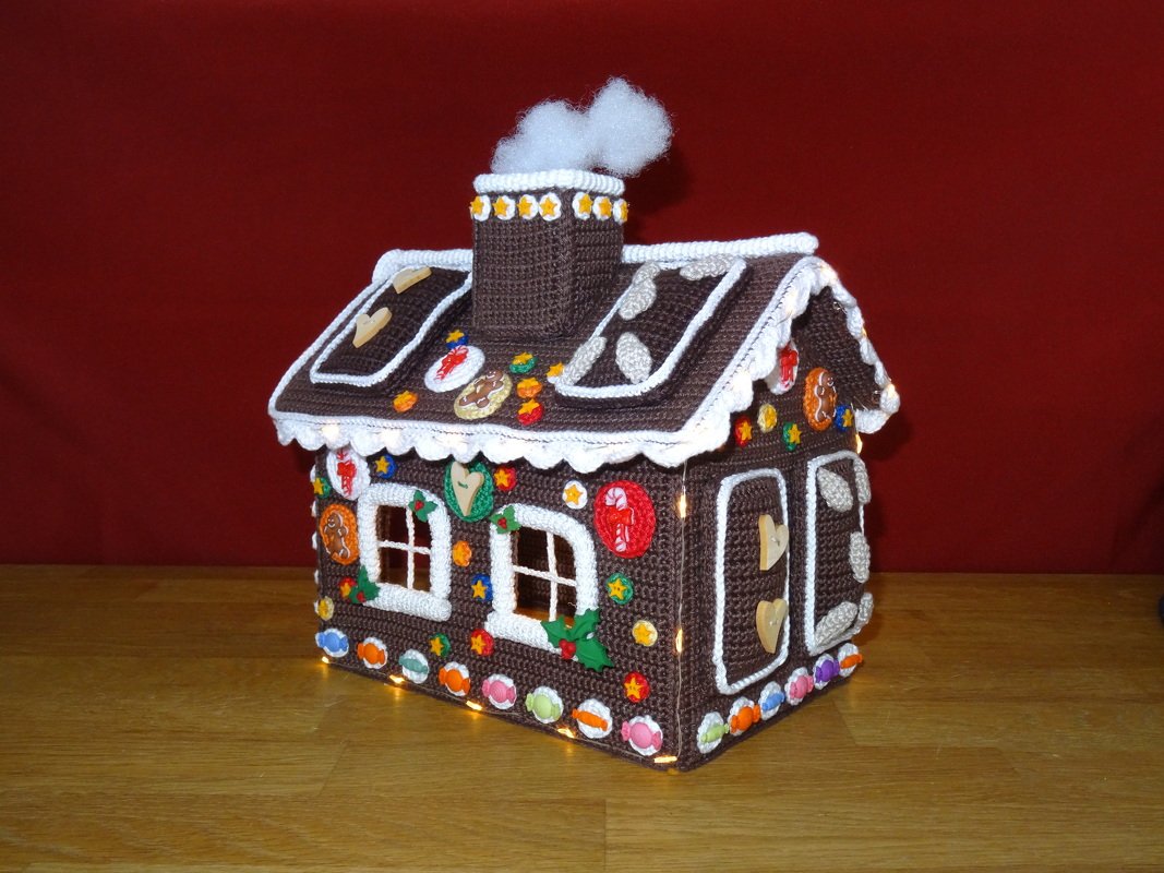 Gehäkeltes Lebkuchenhaus in Braun mit weißer Borte, bunten Knöpfen und Lichterkette