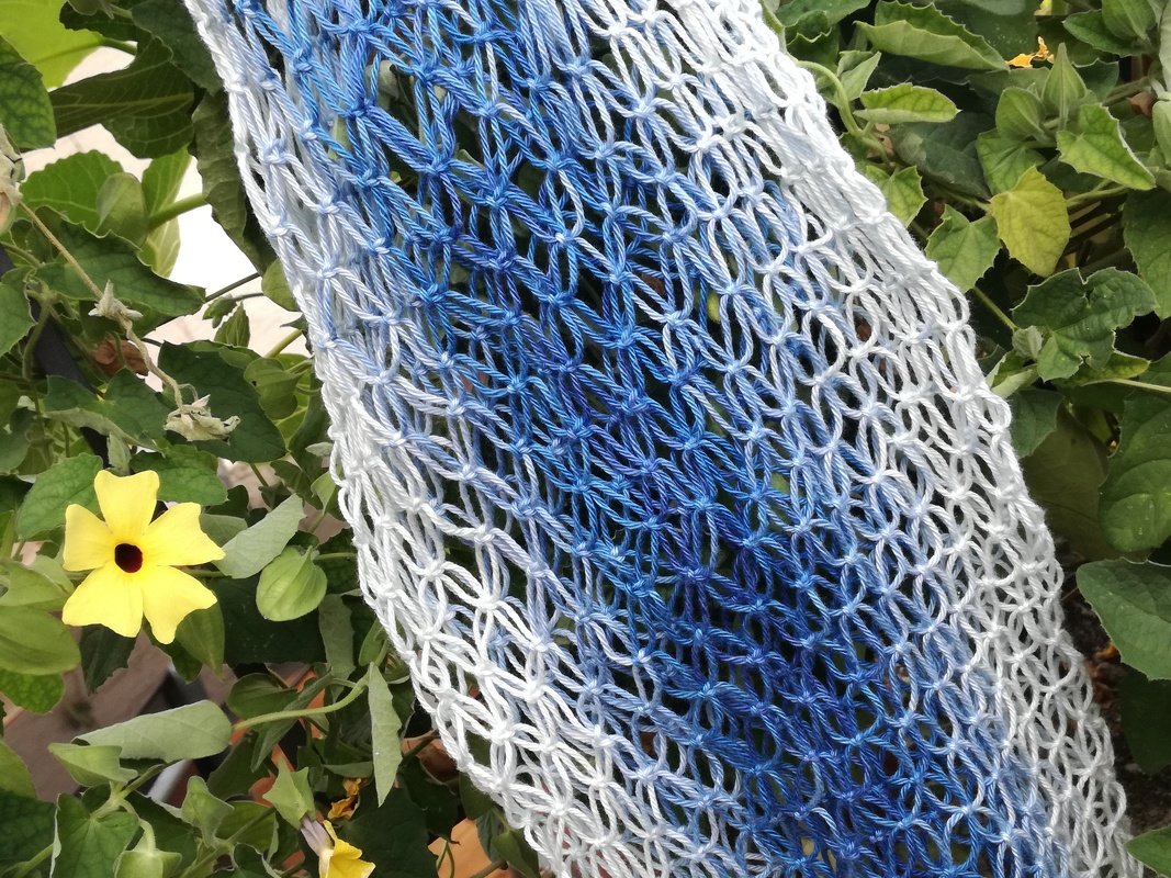 Detail eines offenen Makramee-Musters mit blauen und weißen Schlaufen vor grünen Blättern