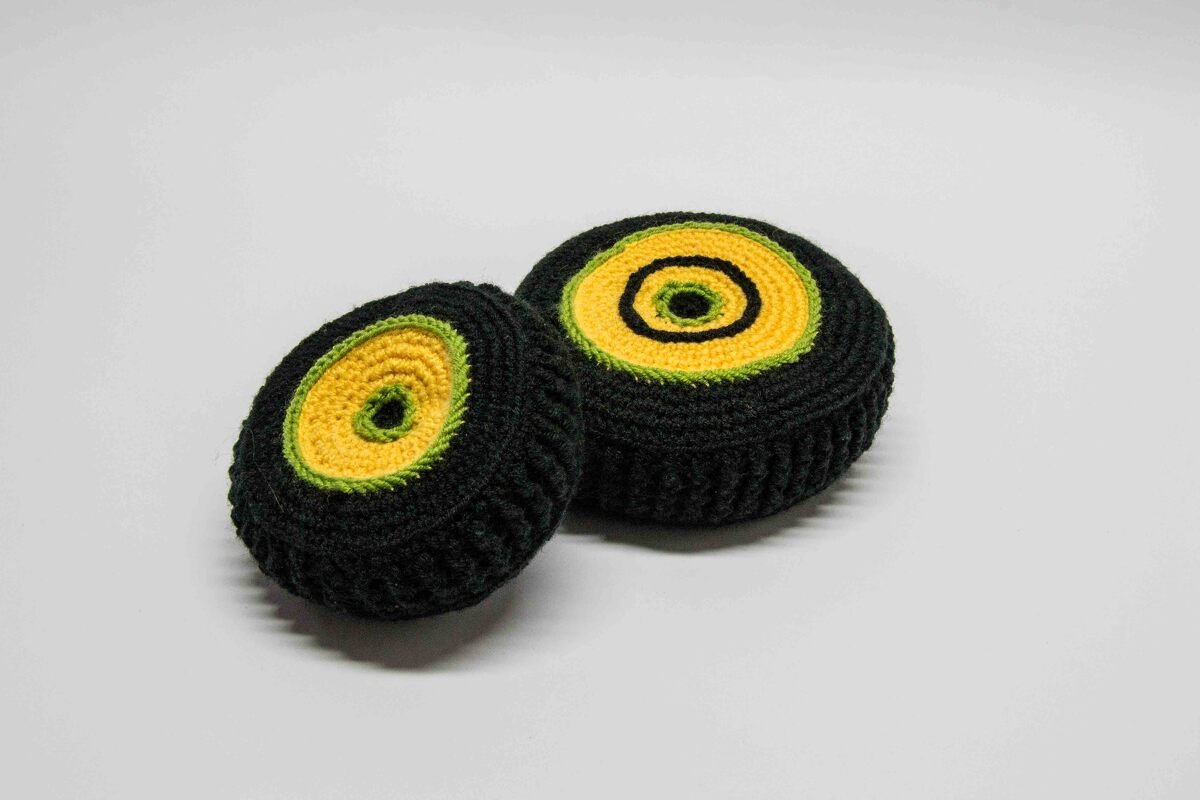 Two crocheted round toys in black, yellow, and lime green concentric circles on a white background.
