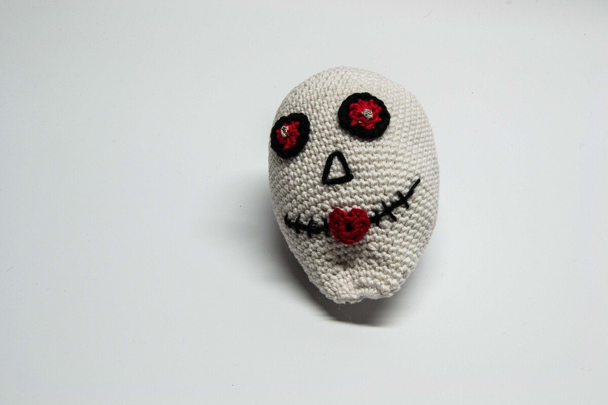 Beigefarbener gehäkelter Totenkopf mit schwarzen Augenringen und herzförmigem roten Mund