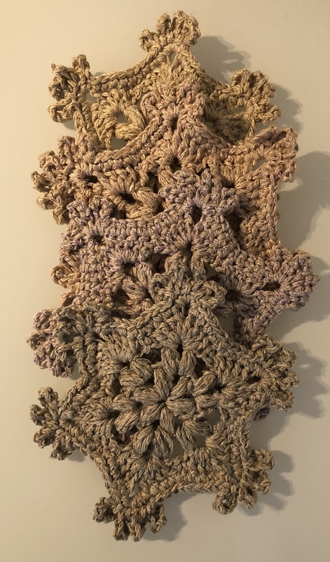 Vertikale Girlande aus gehäkelten, beigefarbenen Schneeflockenmotiven mit sichtbarer Struktur