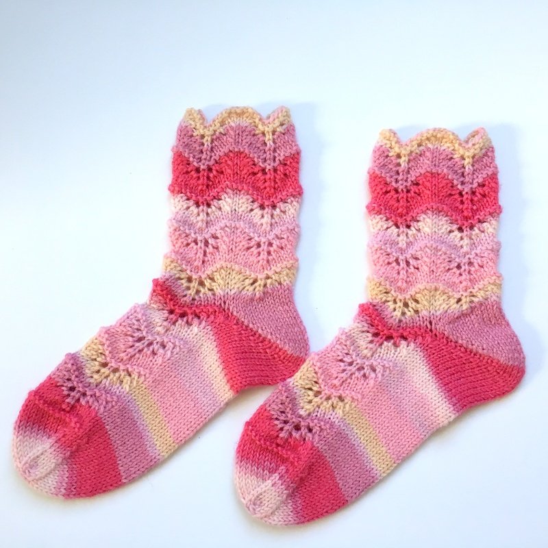 Paar gestrickter Kindersocken in Pink-, Rosa- und Beigetönen mit Wellen- und Lochmuster.