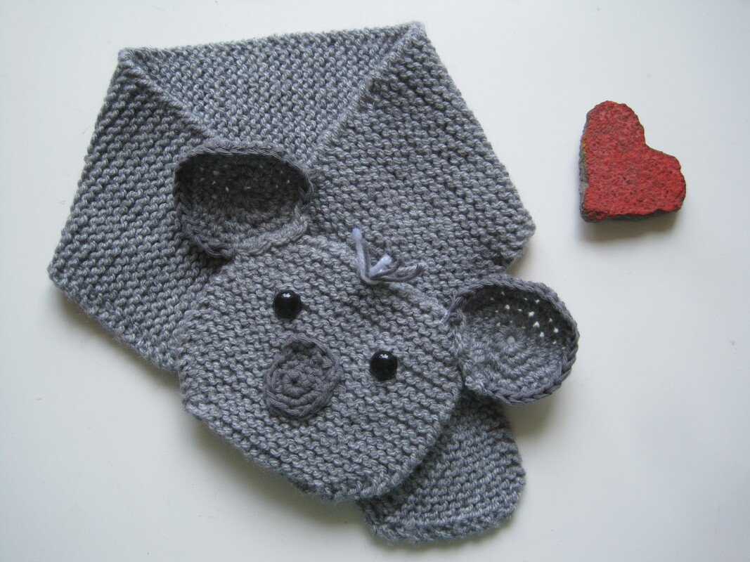 Grau gestrickter Elefantenschal mit Ohren und dunklen Knopfaugen, daneben ein rotes Herz
