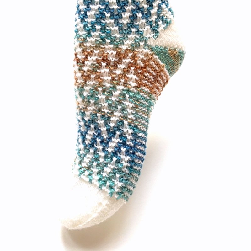 Handgestrickte Damensocke mit blau-türkis-braunem Muster und weißen Akzenten auf weißem Hintergrund.