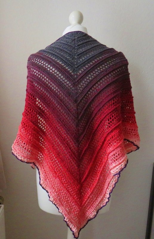 Gehäkeltes dreieckiges Tuch mit Farbverlauf (Grau–Violett–Rot–Pink) auf einer Schneiderpuppe.