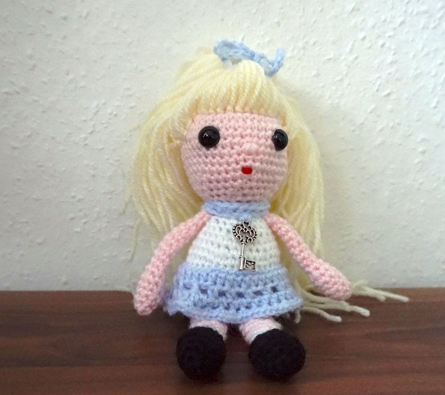 Gehäkelte Amigurumi-Puppe mit hellblondem Garnhaar, blau-weißem Kleid und kleinem Schlüsselanhänger