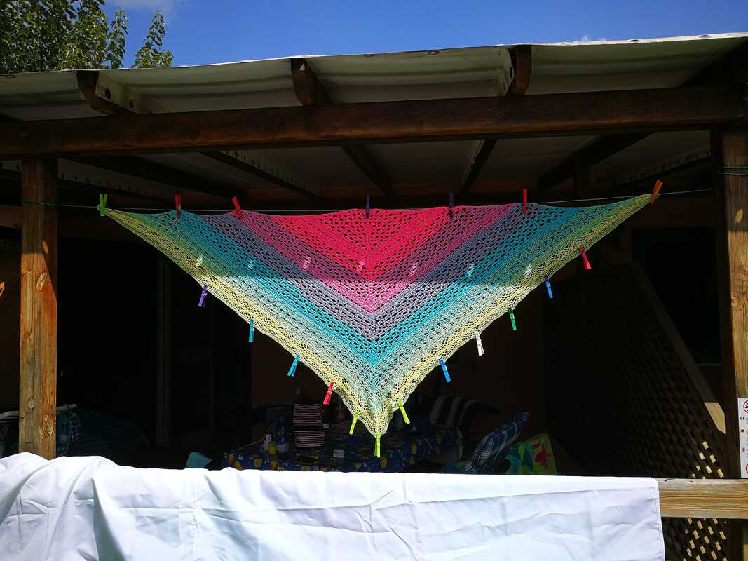 Gehäkeltes Dreieckstuch mit Farbverlauf von Pink über Blau zu Gelb, an einer Leine mit Wäscheklammern gespannt