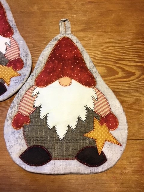 Topflappen mit genähter Weihnachtswichtel-Applikation, roter Mütze, weißem Bart und gelbem Stern auf Holzuntergrund