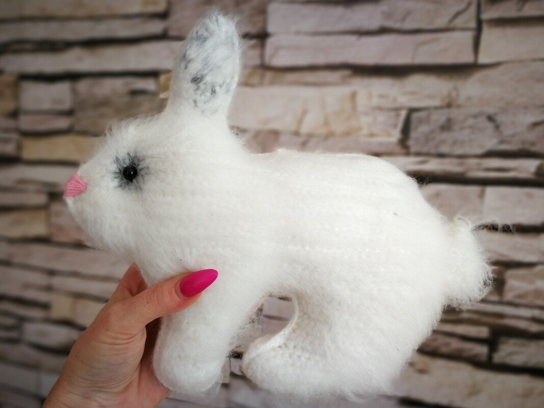 Weißer gehäkelter Amigurumi-Hase mit rosa Nase und grauen Ohren, in einer Hand gehalten