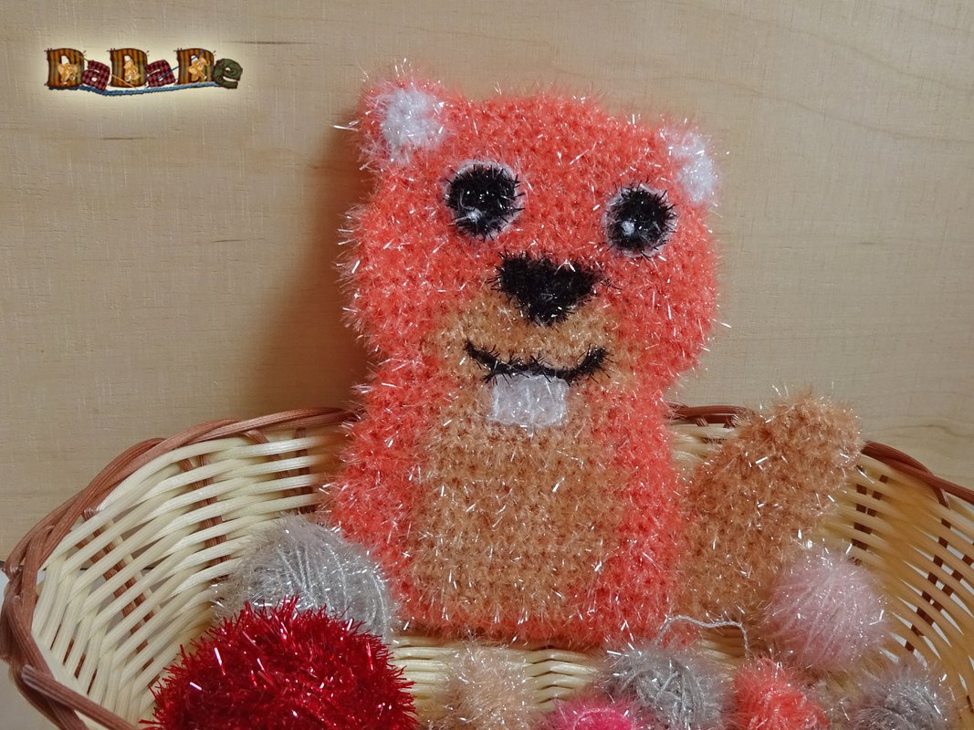 Gehäkelte Tierfigur in Orange und Beige mit flauschiger, schimmernder Struktur, sitzend in einem Weidenkorb mit Dekokugeln.