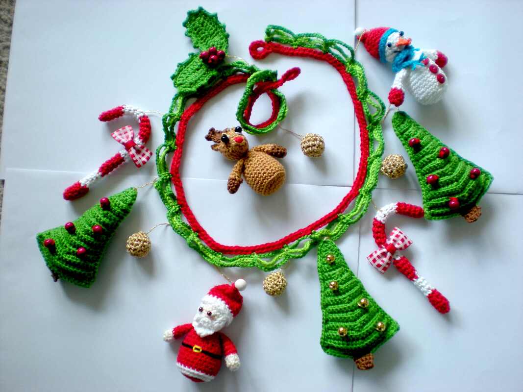 Anordnung gehäkelter Weihnachtsfiguren und -elemente: Rentier, Weihnachtsmann, Schneemann, Tannenbäume, Zuckerstangen, goldene Kugeln und Girlande.
