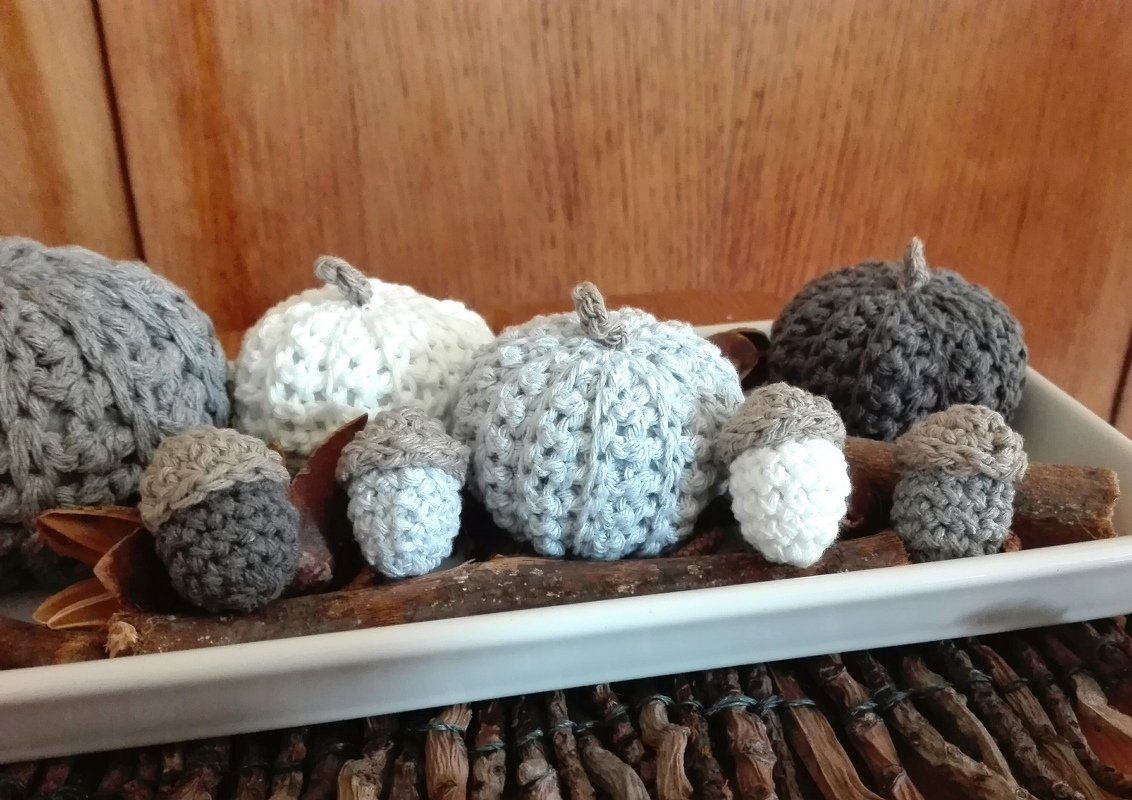 Mini-Kürbisse und Eicheln gehäkelt in Grau und Weiß, arrangiert in einer Schale