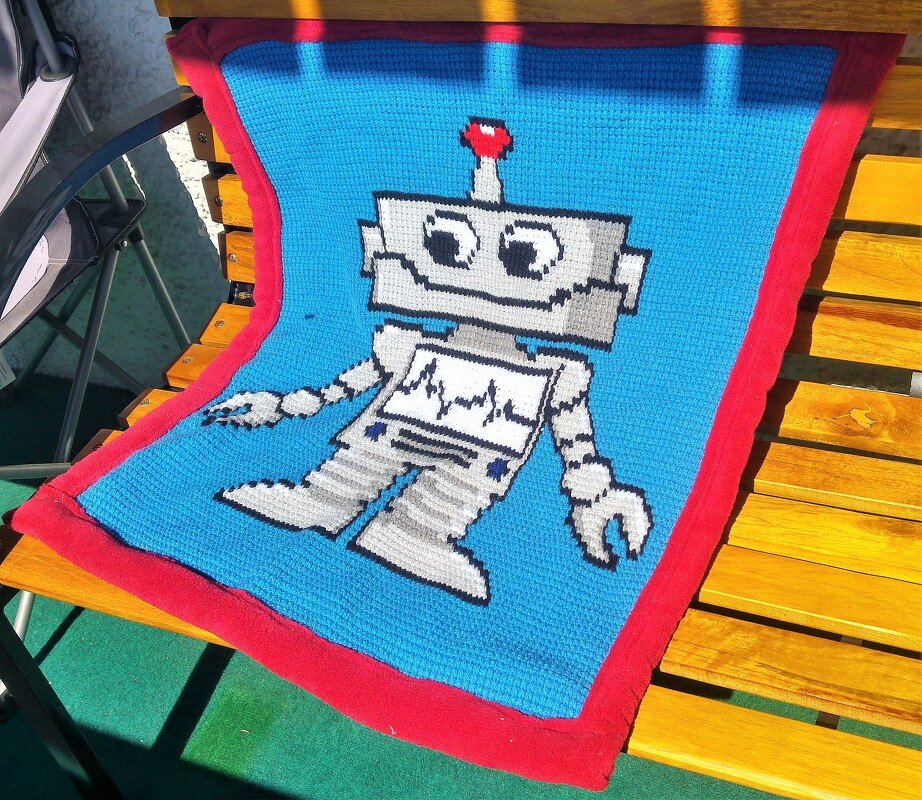 Gehäkelte Babydecke, blau mit rotem Rand und weiß-grauem Pixel-Roboter