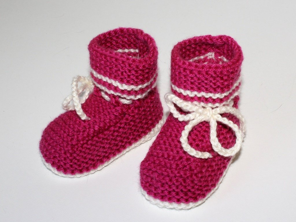 Paar pinker gestrickter Babyschuhe mit weißer Umrandung und Bindeschnur