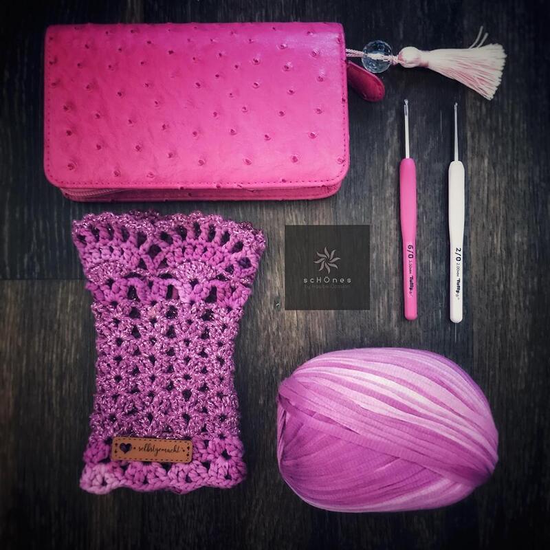 Häkelset mit Armstulpe aus Verlaufsgarn, Knäuel, zwei Häkelnadeln und rosa Geldbörse auf Holzgrund