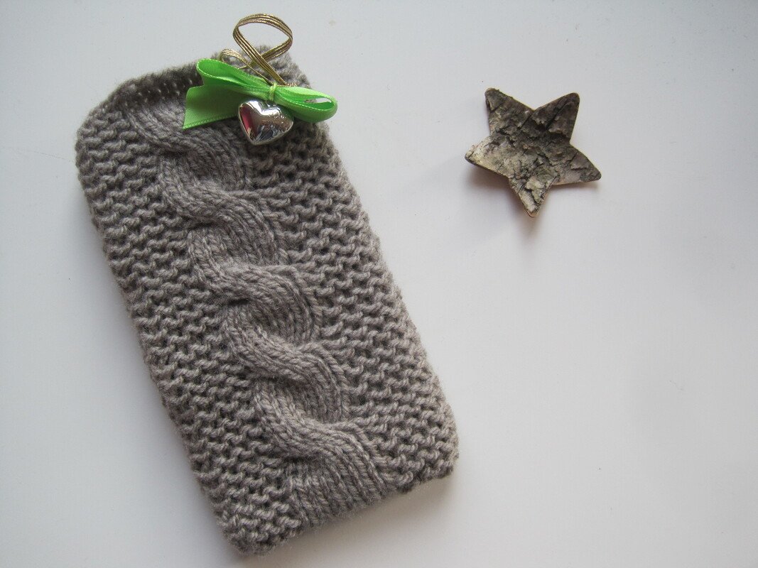 Gestrickte graue Hülle mit Zopfmuster und grünem Band, daneben ein Holzstern