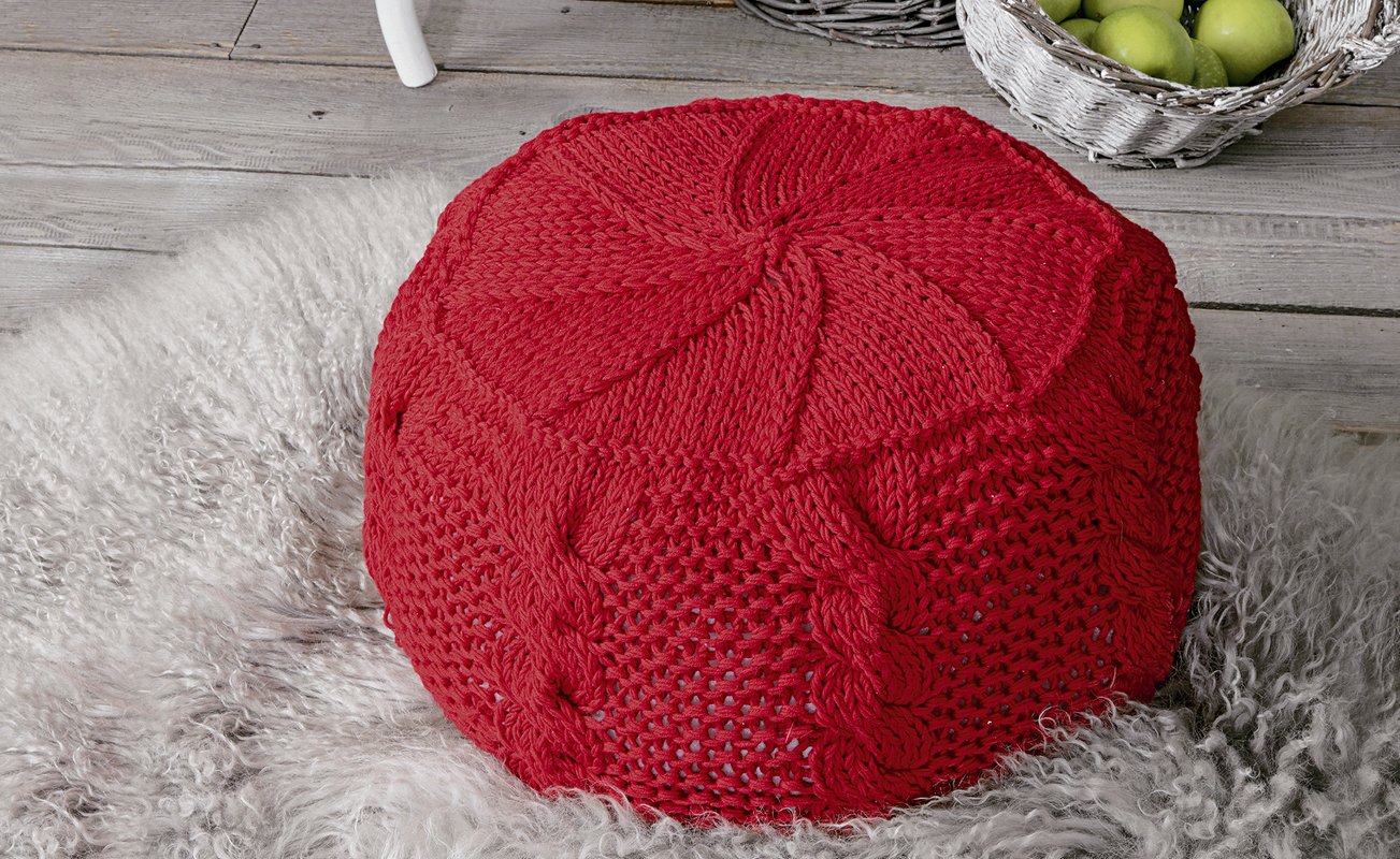 Roter, runder Strickpouf mit Zopf- und Spiralmuster auf hellem Teppich