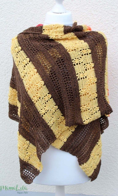 Handgehäkelter Schal auf Schneiderpuppe, diagonal gestreift in Braun und Gelb mit Blumenakzenten.