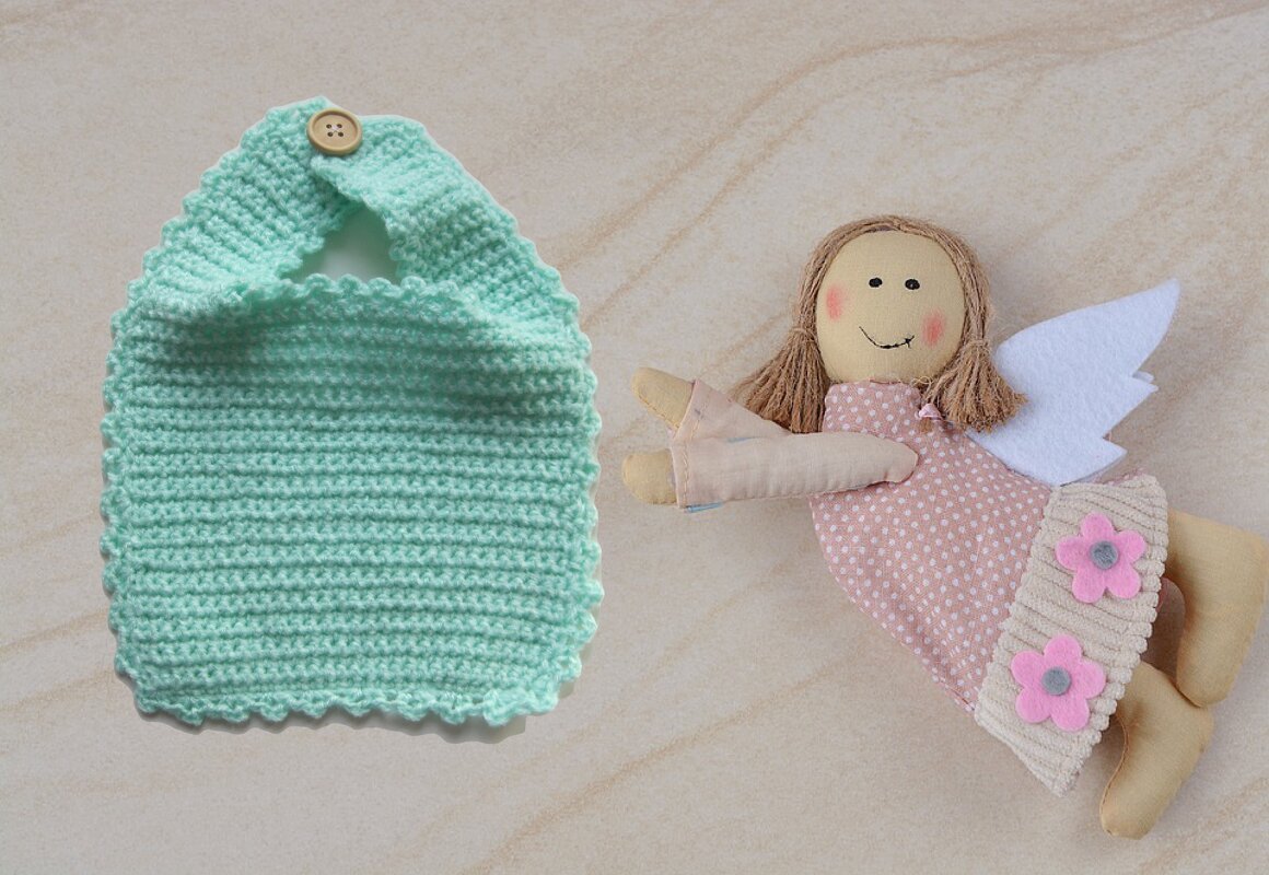 Mintfarbenes schnell gehäkeltes Baby-Lätzchen mit Knopfverschluss neben einer Stoffpuppe