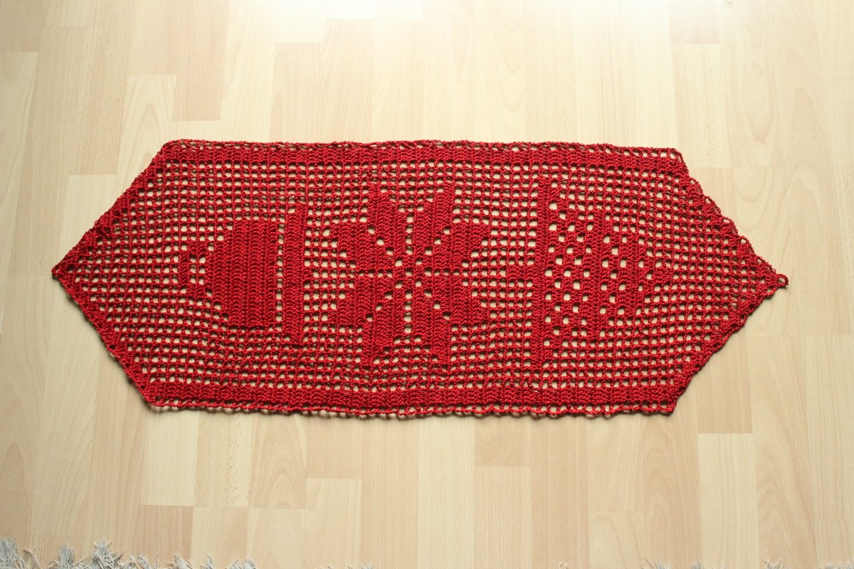 Roter gehäkelter Tischläufer mit LOVE‑Schriftzug und Schneeflocke auf hellem Holzboden