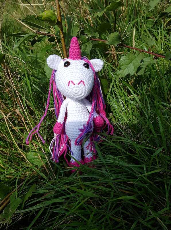 Gehäkeltes weißes Einhorn mit pink‑lila Mähne im Gras