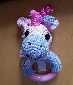 Gehäkelter Einhorn-Greifring in Pastellfarben auf Holzuntergrund