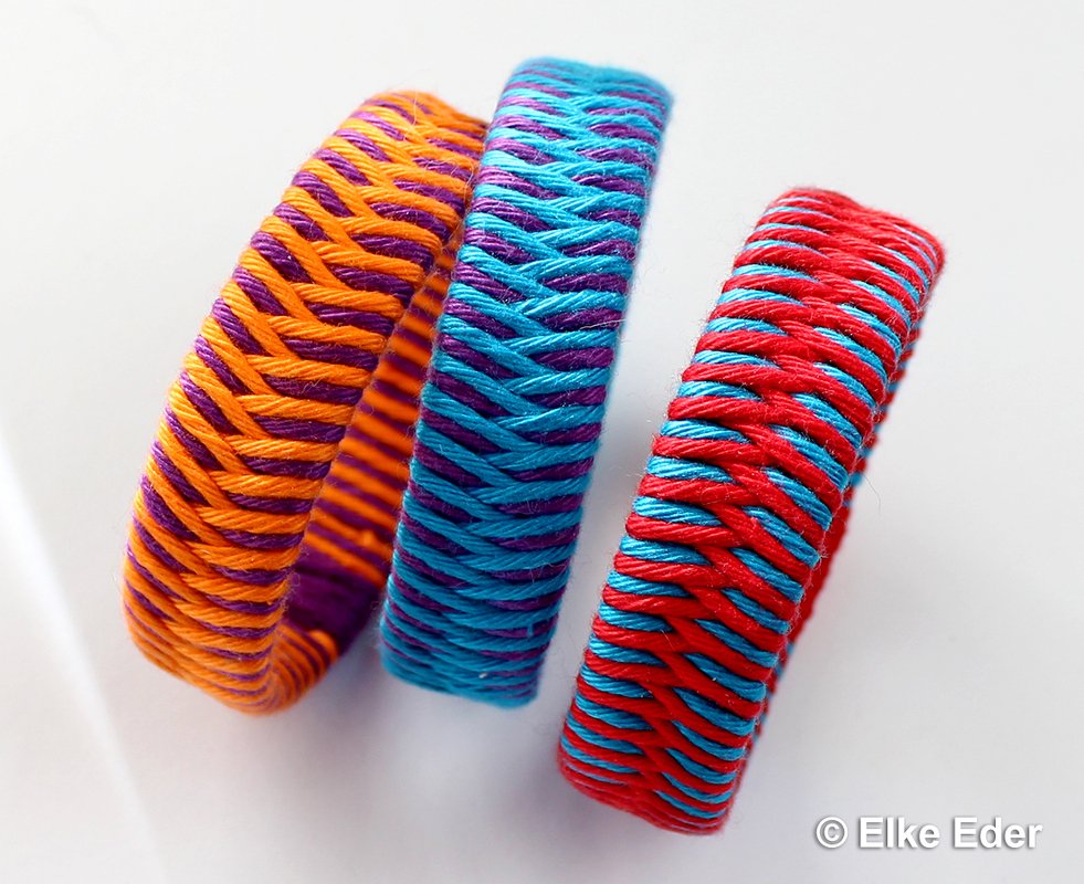 Drei bunte eng gewickelte Armbänder mit Flechtmuster auf hellem Hintergrund