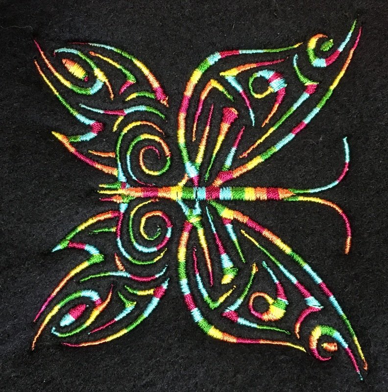 Bunte Schmetterling-Stickerei mit Tribal-Mustern in Regenbogenfarben auf dunklem Stoff.