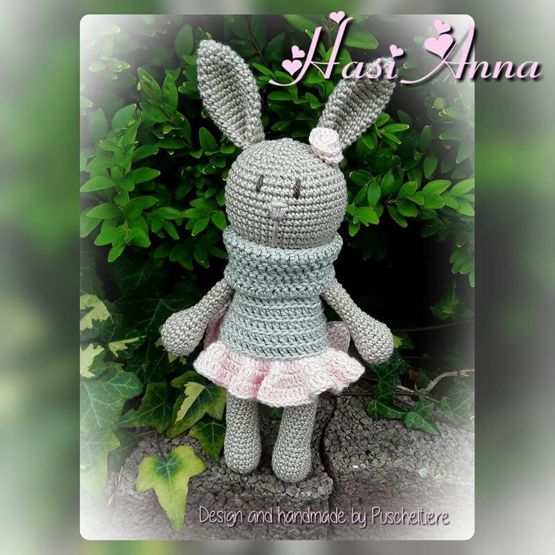 Graues Amigurumi-Häschen mit rosa Rüschenrock und Schal, vor grünen Blättern