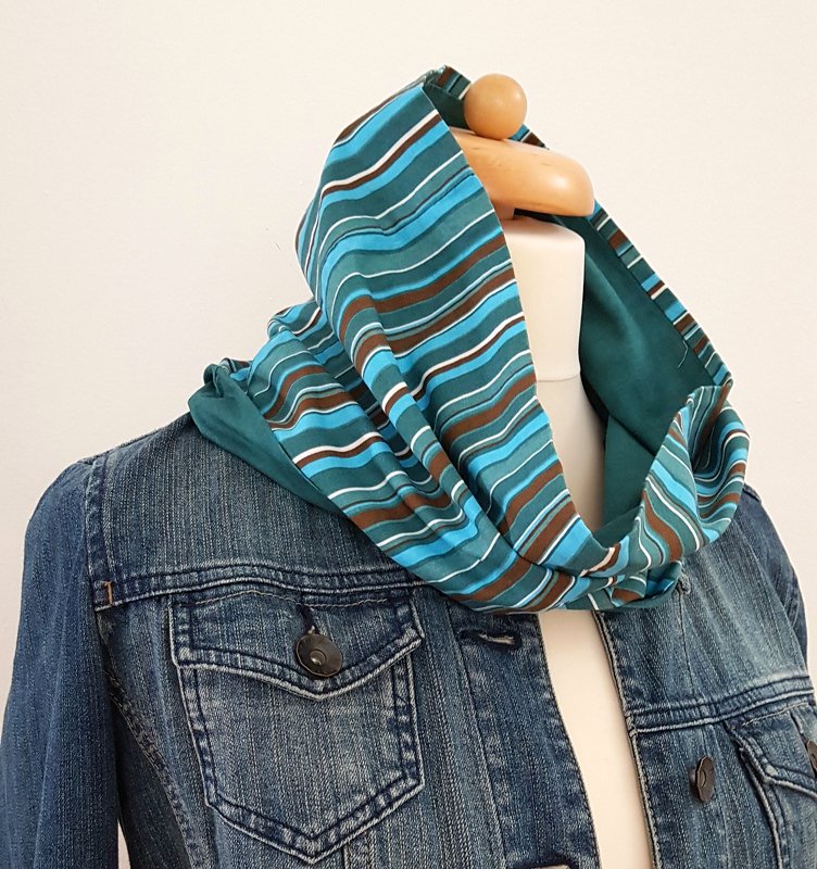 Gestreifter Loopschal in Blau- und Brauntönen auf einer Schneiderpuppe mit Jeansjacke.