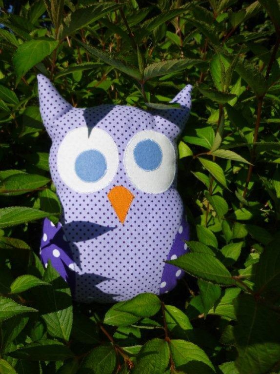 Gepunktete Stoff-Eule mit applizierten weißen Augen und orangefarbenem Schnabel zwischen grünen Blättern