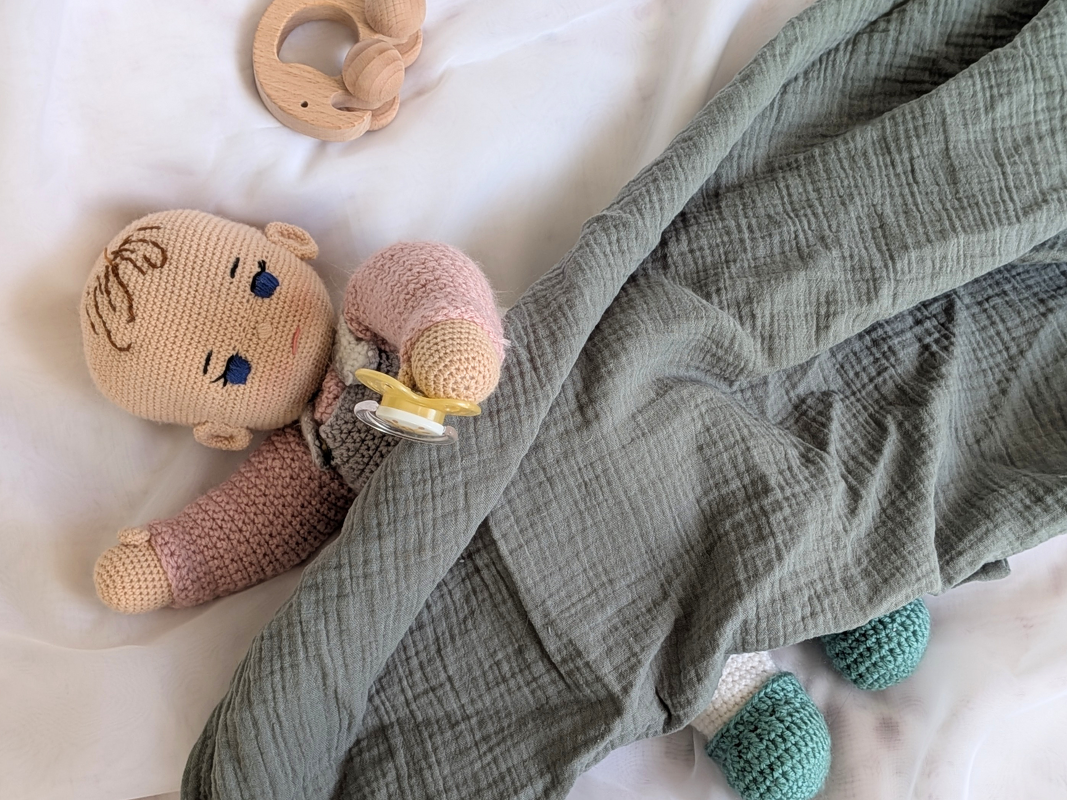 Hand-crocheted amigurumi baby doll with pacifier, sage blanket, and wooden teether