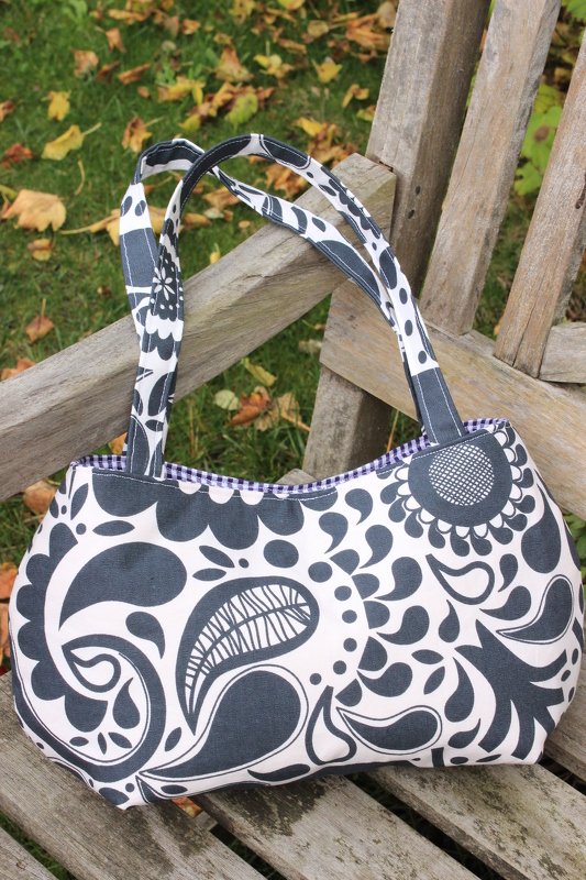 Geräumige Stofftasche mit schwarz-weißem floralen und Paisley-Muster auf einer Holzbank