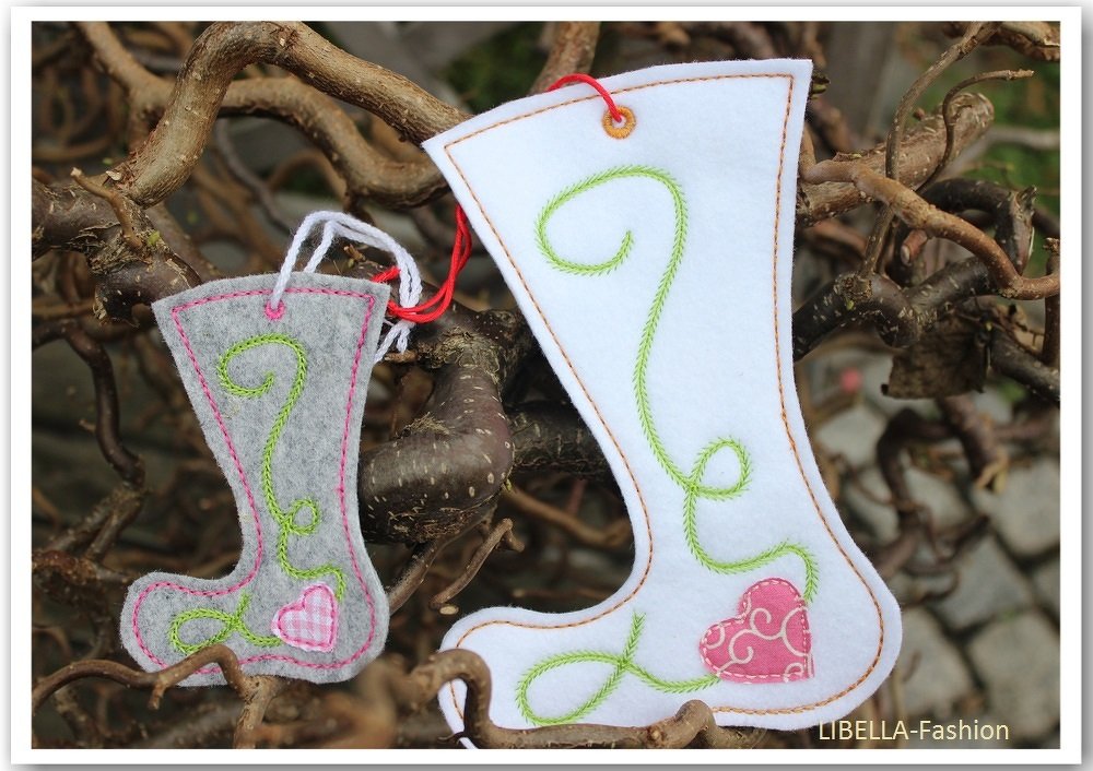 Zwei bestickte Filzstiefel-Anhänger in Weiß und Grau mit grüner Sticklinie und pinkem Herz, an Zweigen hängend