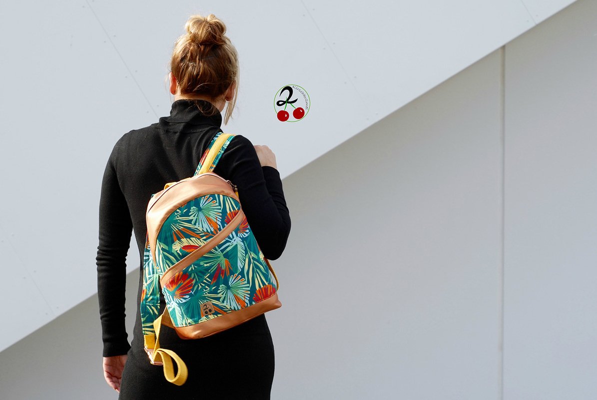 Person von hinten trägt kleinen Rucksack mit tropischem Blattmuster und braunen Besätzen