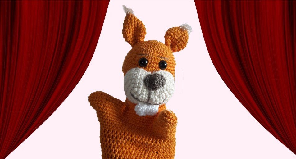 Gehäkelte orangefarbene Handpuppe mit weißer Schnauze vor roten Vorhängen