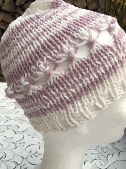 weiß und pastellrosa gestreifte Strickmütze mit Rippenbund und dekorativen Knotenreihen auf Schaufensterkopf