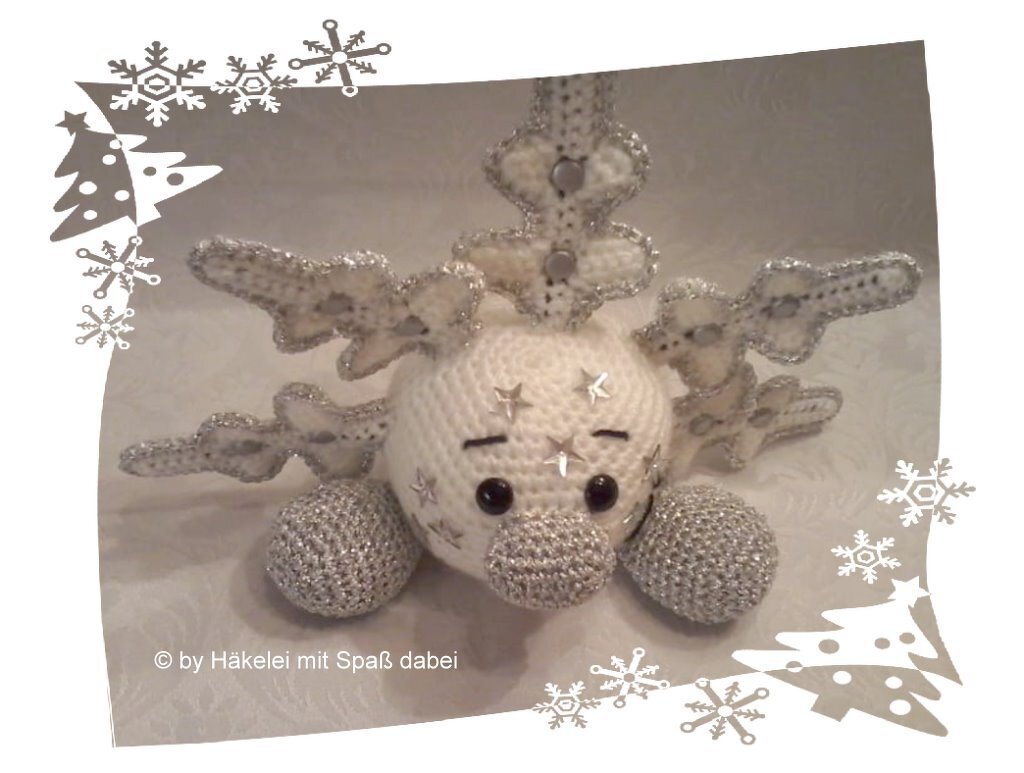 Weißes gehäkeltes Rentier‑Amigurumi mit silbernen Glitzerrändern an Geweih, Nase und Füßen und Sternverzierungen