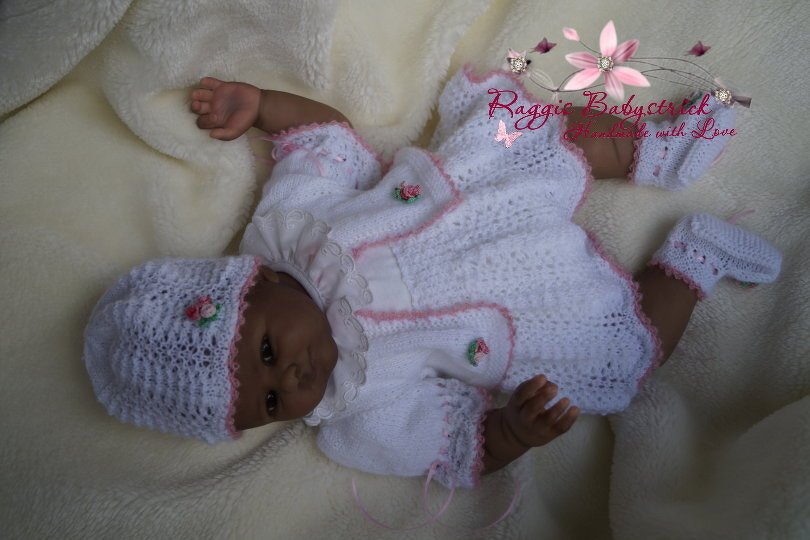Weiß-rosa gestricktes Babyensemble mit Lochmuster und Rosenapplikationen auf Babypuppe