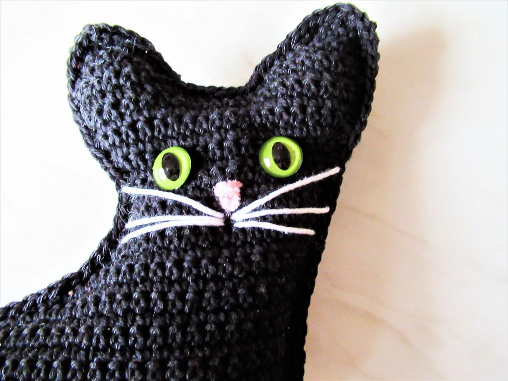 Schwarze gehäkelte Katze mit grünen Augen und rosa Nase