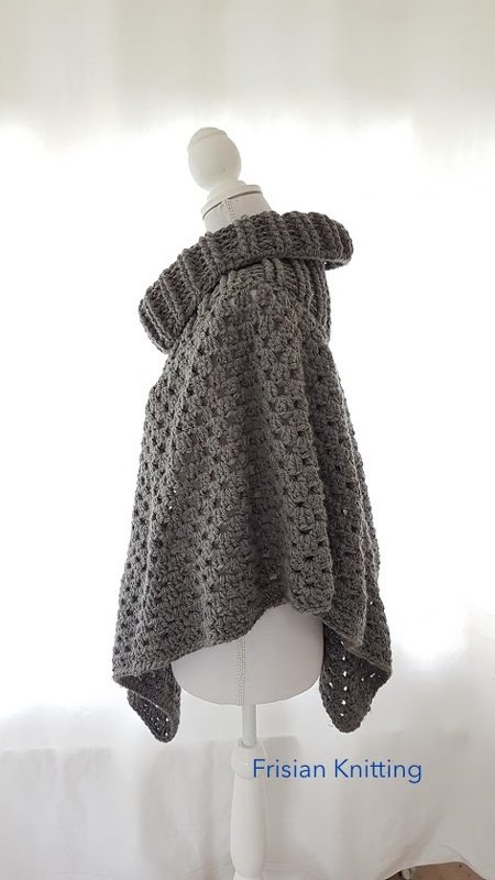 Dunkelgrauer Häkelponcho mit hohem Rollkragen auf weißer Schaufensterpuppe, seitliche Ansicht.