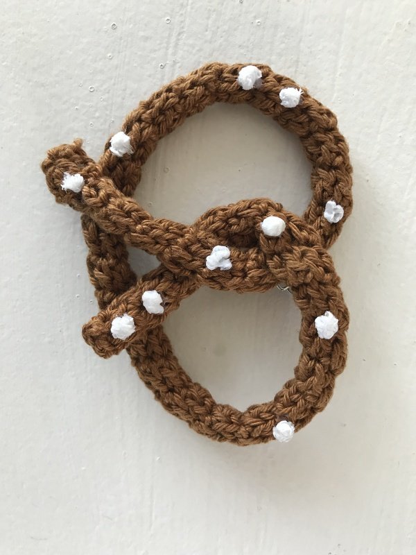 Braune gehäkelte Brezel mit weißen Punkten auf hellem Hintergrund.