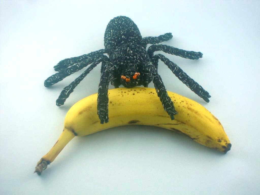 Gehäkelte schwarze Spinne mit orangefarbenen Augen auf einer gelben Banane