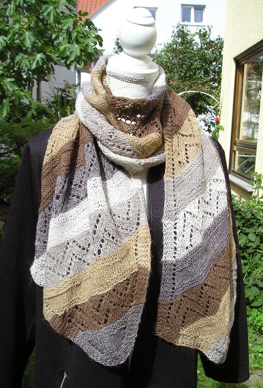 Gestrickter Schal in Erdtönen mit diagonalen Streifen und zartem Lochmuster an einer Schaufensterpuppe.