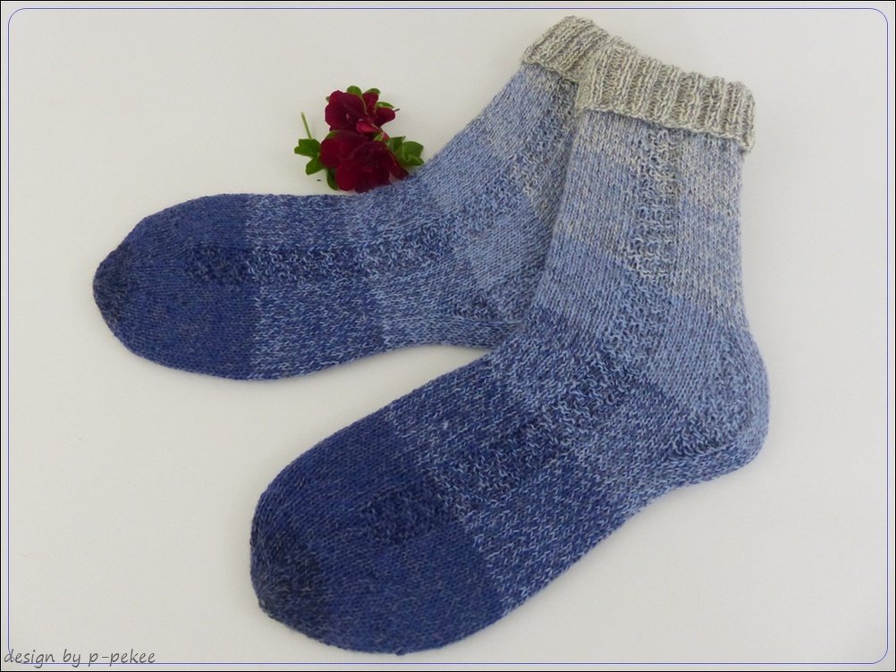 Paar handgestrickter kurzer Socken in melierten Blautönen mit hellgrauem Rippenbündchen, dekorativ mit kleiner Blüte auf weißem Hintergrund