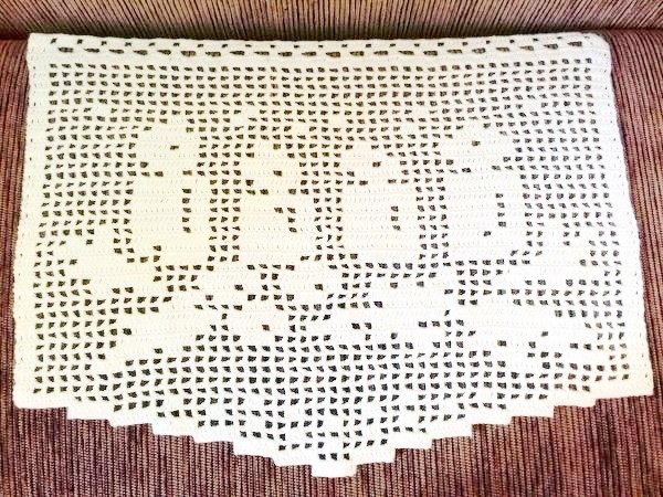 Weißes Filet‑Häkelstück mit dem Schriftzug JOY und Sternmotiven auf rötlich‑braunem Stoffuntergrund