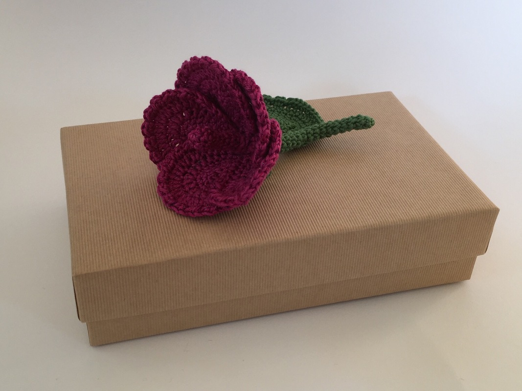 Schnell gehäkelte pinke Blume mit grünem Stiel auf brauner Schachtel