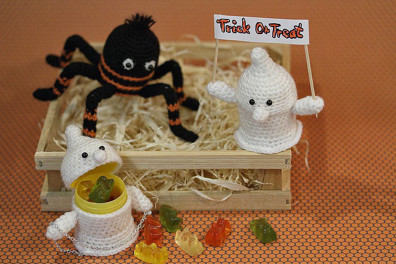 Drei gehäkelte Halloween-Figuren: weißes Gespenst mit Schild, Gespenst-Behälter mit Gummibärchen und schwarz-orange Spinne